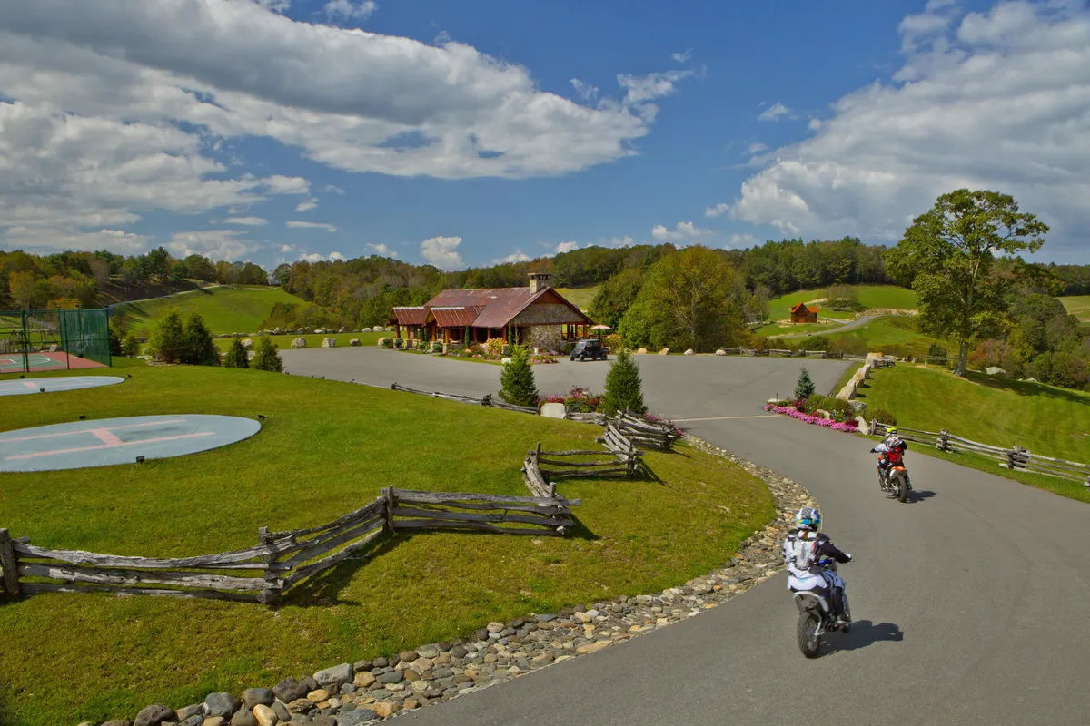 This image features a spacious green lawn in front of a rustic lodge, with visible basketball court and several motorcycles parked along the road. The scene is lively and family-oriented, hinting at outdoor sports and barbecues, with enough space for children to play and families to gather.