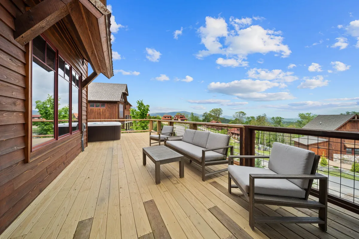 A calm and inviting deck area with comfortable seating and a hot tub, overlooking a stunning scenic view. The setting is peaceful, ideal for relaxation after an action-packed day, and features enough space for socializing or soaking under the stars.