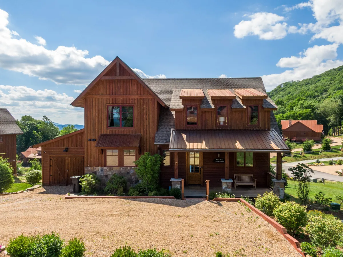 The image showcases the exterior of a charming wooden single-family house nestled in the mountains of Banner Elk, North Carolina. The inviting front porch is surrounded by tasteful landscaping, offering comfortable seating to enjoy expansive sunset views. The scene suggests a cozy, welcoming atmosphere perfect for relaxing or gathering with friends and family in a tranquil mountain setting.