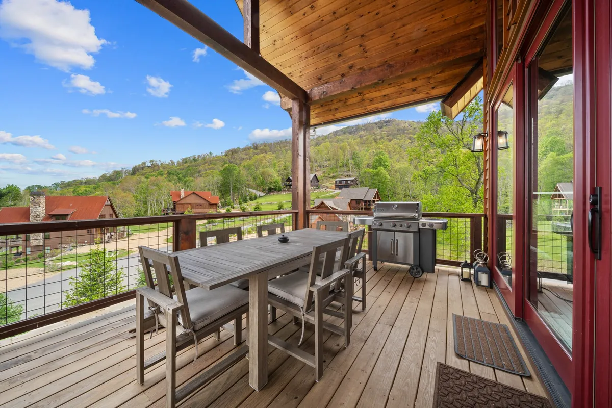 An exterior view of the deck set for outdoor dining, with a dining table, gas grill, and sweeping mountain views in the background. The setting is ideal for barbecues, sunset meals, or stargazing with friends and family.