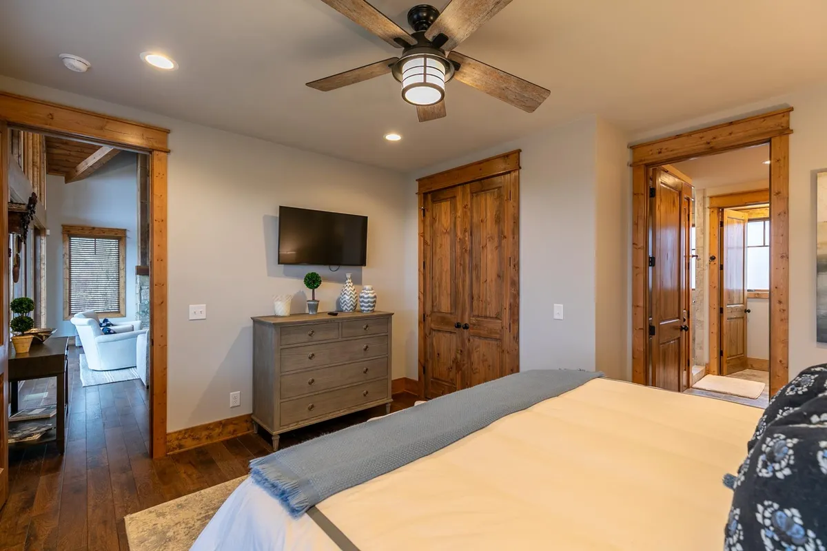 A comfortable bedroom featuring a light-colored bed, a wooden dresser, and a wall-mounted television. The space is bright and airy, perfect for unwinding with a movie or enjoying a peaceful morning.