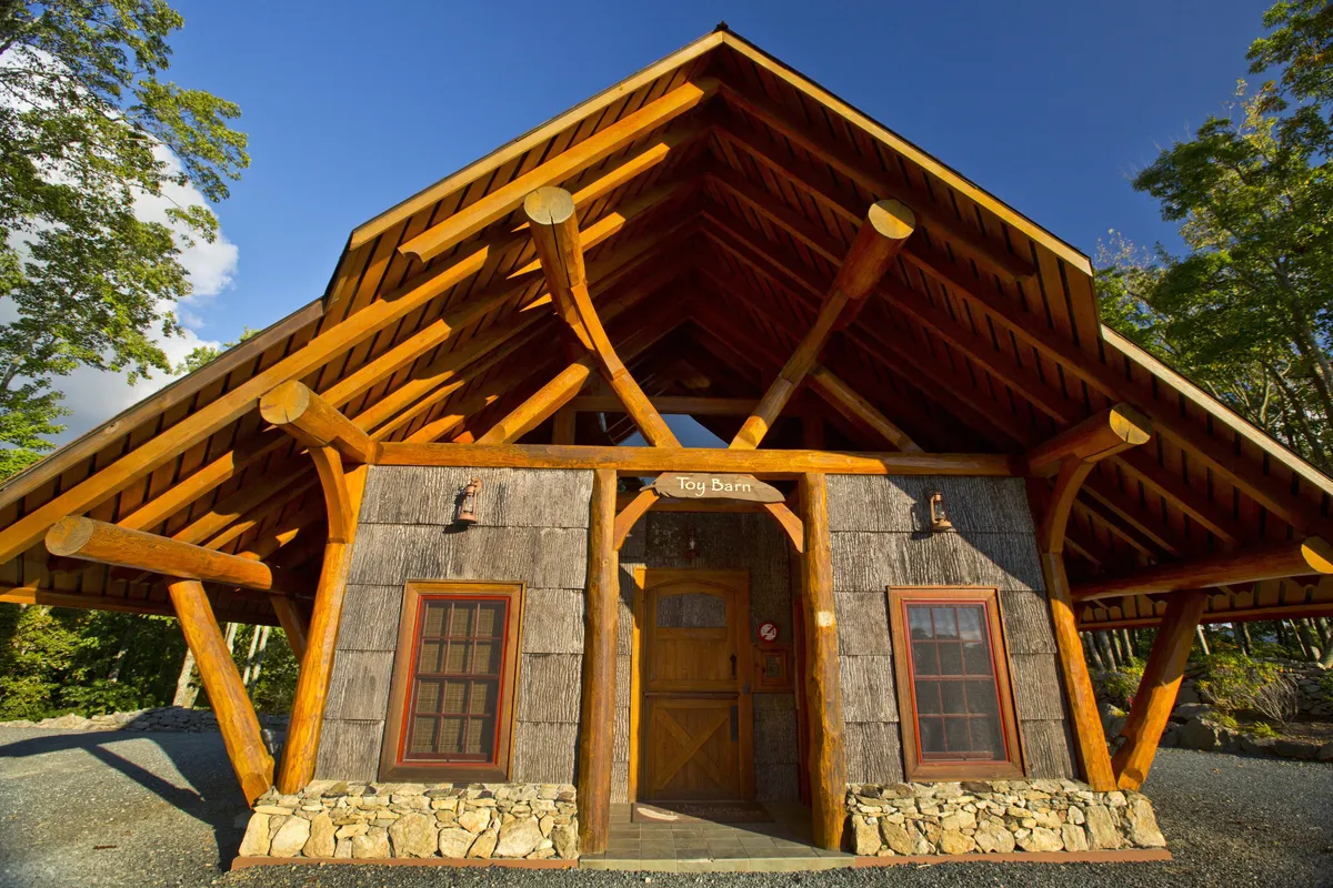 The photo shows a log-constructed building with a large overhanging roof and a front door with clear signage. The atmosphere is informal and playful, with open space out front for outdoor play, gatherings, or creative activities.