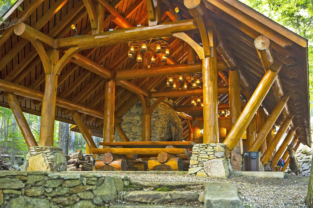 This inviting outdoor gathering space features wooden beams, a stone fireplace, hanging lanterns, and a large wooden table. The communal setup and fire table evoke evenings spent relaxing outdoors, providing a perfect spot for both guests and their dogs to wind down after a day of adventure.