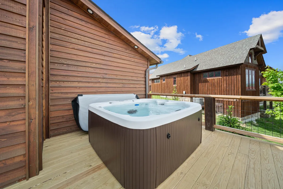 A tranquil view of the outdoor deck featuring a bubbling hot tub and the surrounding lodge architecture. The scene invites relaxation and socializing after a meal, with space for guests to unwind amid mountain air.