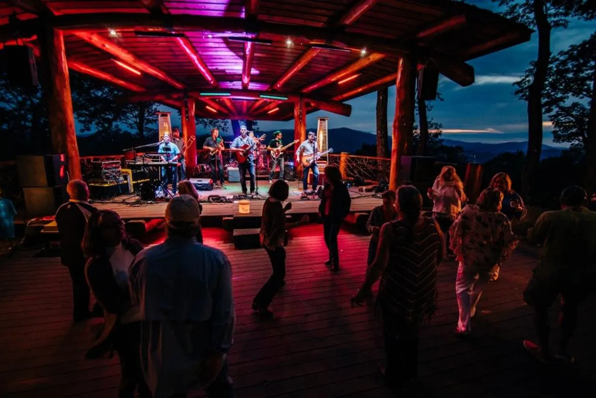 A dynamic scene of a crowd gathered at an outdoor stage with performers and colorful lighting, embodying the energy of live music events and summer amphitheater gatherings within the community.