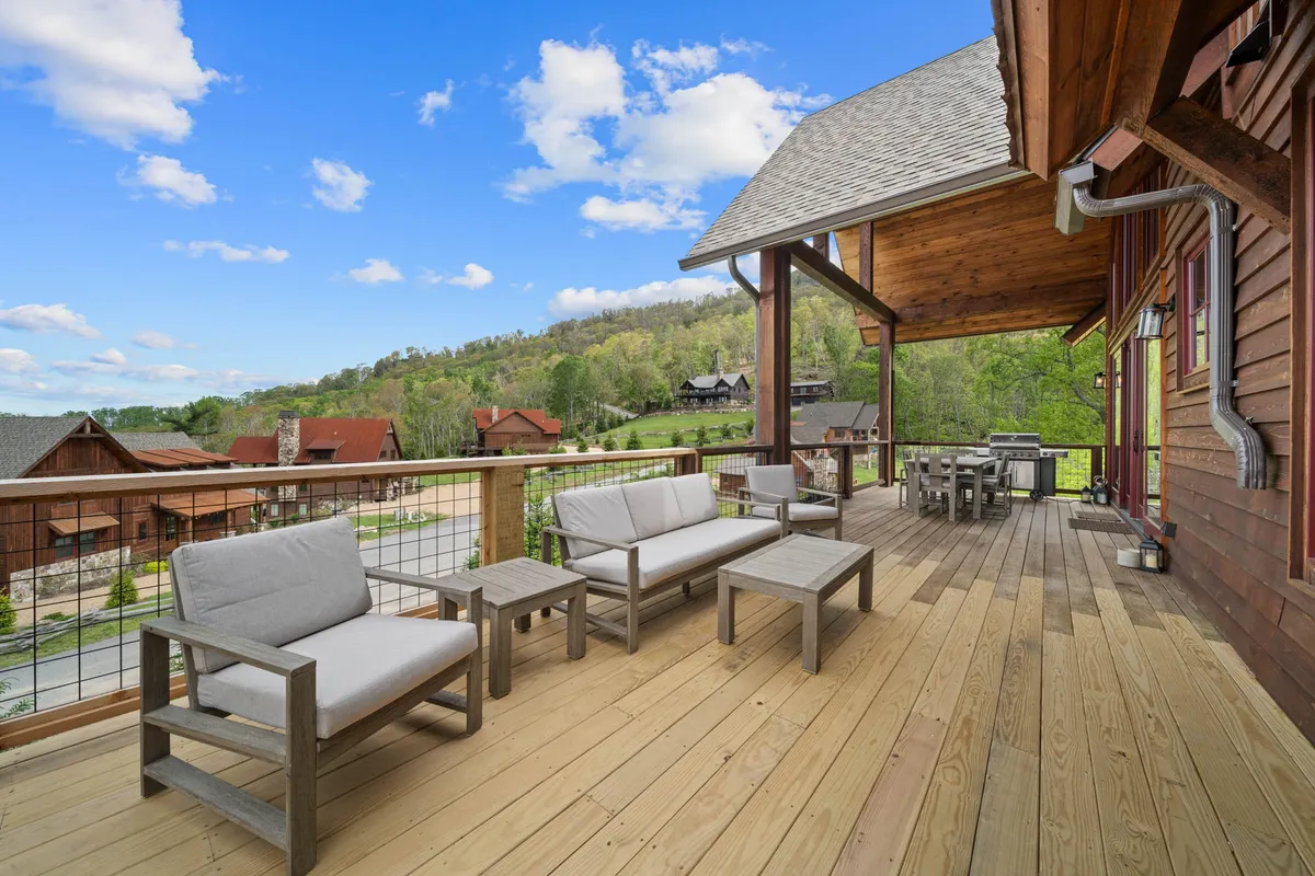 This image features a spacious outdoor seating area with a dining table set on a wooden deck, surrounded by a scenic mountain landscape. The setting is designed for relaxation, social gatherings, and enjoying meals while taking in the expansive views. The tranquil atmosphere is enhanced by the mountain backdrop and the inviting arrangement of the furniture.