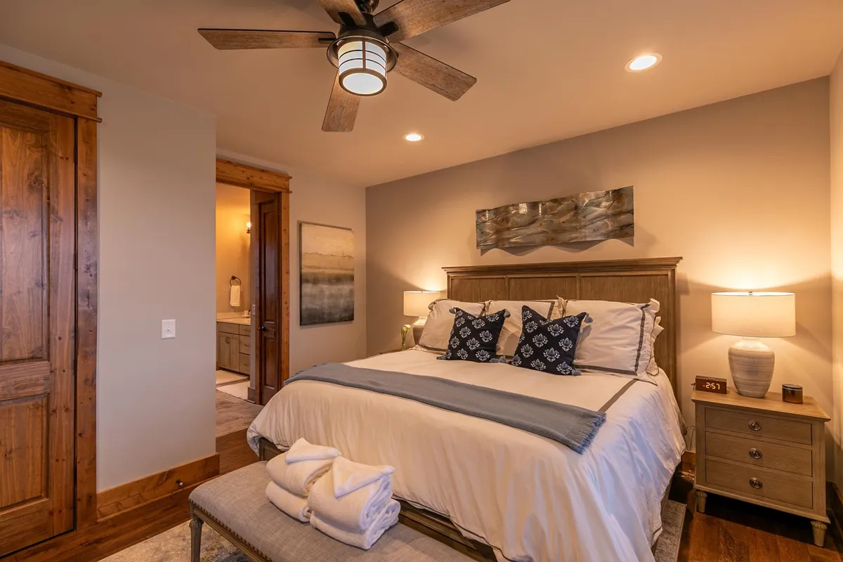 A tranquil bedroom with a plush bed adorned with decorative pillows, nightstands with lamps on each side, and soothing artwork on the wall. Natural light floods in, enhancing the room's peaceful and restful ambiance.