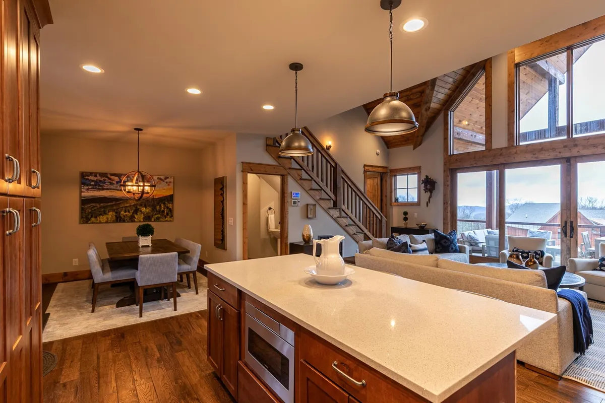 A wide-angle view of the open-concept dining and kitchen area, featuring the kitchen island, an adjacent dining table, and a glimpse into the cozy living space. Large windows flood the space with natural light, and the arrangement encourages communal dining and lingering conversations.